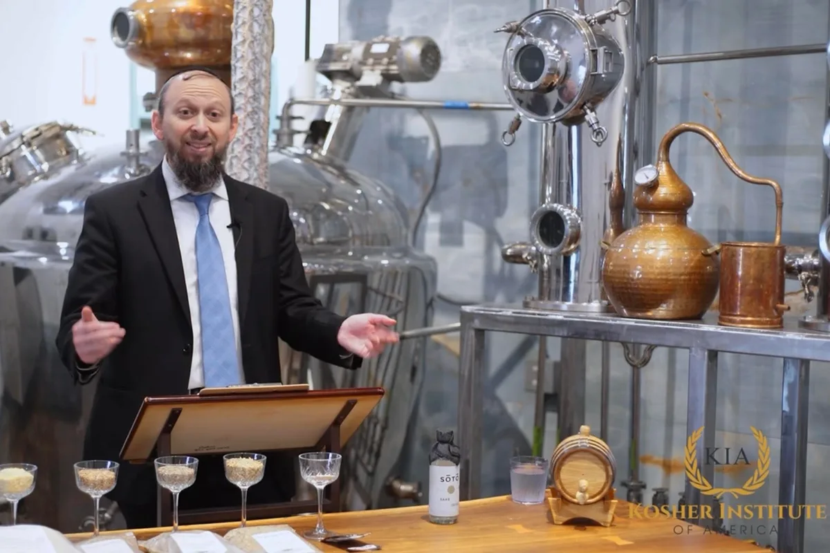 Rabbi Akiva Niehaus teaches the Kosher Liquor Masterclass from a lectern on a distillery floor, tasting glasses and a copper still beside him.